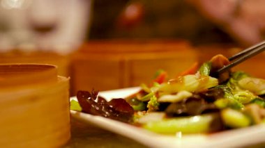 Çubuklar tabaktan rengarenk kızarmış sebze topluyor. Ilık aydınlatma sıcak bir yemek atmosferi yaratır.