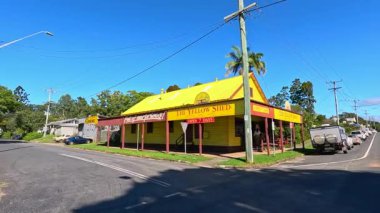Güneşli bir günde canlı sarı bir hediyelik eşya dükkânı. Sakin bir caddede geçen araçlar.