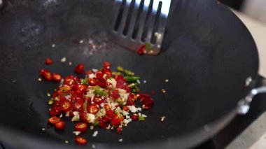 Tavada doğranmış biber ve sarımsak karıştırılmış spatula yakın plan. Parlak ışıklandırma canlı renkleri ve dinamik pişirme eylemini vurguluyor