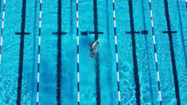 Drone, güneşli bir yüzme havuzunda serbest yüzme alıştırması yapan bir yüzücüyü yakalıyor, ritmik hareketler ve temiz su dokuları sergiliyor.