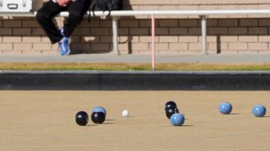 Güneşli bir günde bir çim kasesi oyunu başlıyor, oyuncuları ve kaseleri iyi korunmuş çimlerde sergiliyor.