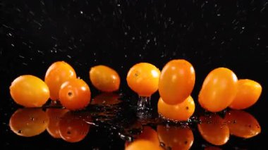 Kiraz domatesleri yavaş çekimde yansıtıcı siyah bir yüzeye düşüp zıplarlar, dinamik ve canlı bir görsel yaratırlar.