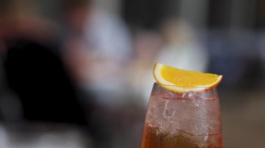 Limon dilimi ile süslenmiş bir Aperol spreyinin yakın plan çekimi, sıcak ışıkta bulanık bir arka plan üzerine kuruludur.