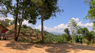 Tayland, Phuket 'te açık mavi bir gökyüzünün altında yemyeşil ve ağaçlarla çevrili kırmızı bir bungalovun sakin bir manzarası.