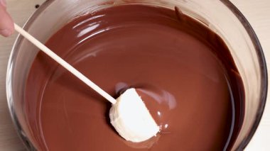 Muz dilimi yumuşak erimiş çikolataya şiş kullanılarak batırılıyor.