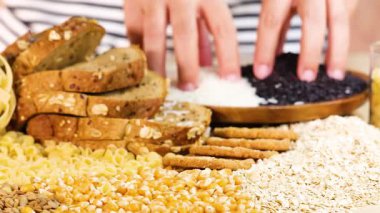 Eller bir masada çeşitli tahıl ve ekmekleri organize eder, parlak ışıklandırmada renkli yiyecek çeşitlerini sergiler