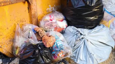 Güneşli bir Phuket caddesinde çöp torbalarıyla dolu taşmış bir çöp konteynırının statik görüntüsü.