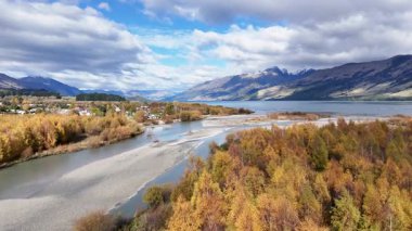 Drone, Glenorchy, Yeni Zelanda 'da canlı bir sonbahar yeşilliği ve dingin bir nehir yakalar. Parlak gün ışığı manzaralı dağ zeminini güçlendirir.
