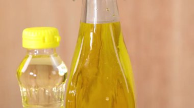 Bir şişe zeytinyağı, bir kase yeşil zeytin ve bir bardak badem yumuşak, doğal ışıklandırma ve yumuşak kamera hareketleriyle hafif ahşap bir yüzeye dizilir.