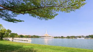 Rama IX Park 'ın Bangkok' taki göletinin sakin bir sahnesinde, yemyeşil ve açık mavi bir gökyüzü gün ışığında ele geçirildi.