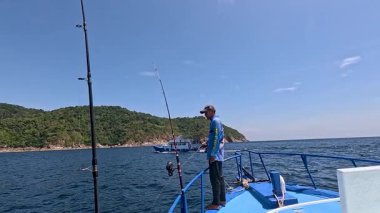 Bir adam açık mavi gökyüzünün altında Tayland, Phuket yakınlarında bir teknede balık tutuyor.