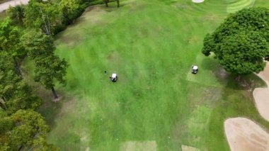 İnsansız hava aracı görüntüleri Phuket, Tayland 'daki yemyeşil bir pistte golfçüleri yakalıyor, canlı manzarayı ve sakin atmosferi vurguluyor.