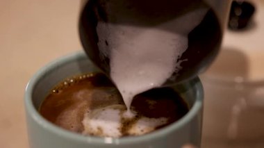 Süt, dumanı tüten bir kahve bardağına dökülür ve girdap şeklinde kıvrılır. Ilık aydınlatma sıcak atmosferi güçlendirir