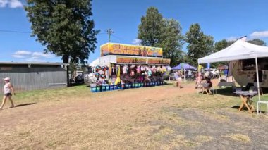 İnsanlar güneşli bir panayırda yürüyor ve eğleniyorlar.