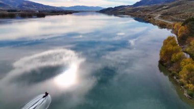 Dunstan Gölü 'nde süzülen bir jet, sonbahar renklerini ve dağları yansıtıyor, dinamik ve dinamik bir manzara yaratıyor.