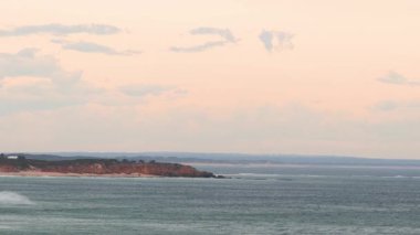 Büyük Okyanus Yolu boyunca sakin bir okyanus manzarası, sakin suları sergiliyor ve günbatımında pastel bir gökyüzü, pürüzsüz bir tavada yakalanıyor.