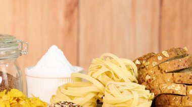 Tahta bir arka planda sergilenen tahıl, makarna ve ekmek çeşitleri.