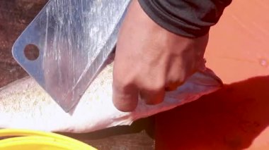 Bir insan güpegündüz tahta bir yüzeyde satırla ustaca balık temizler.