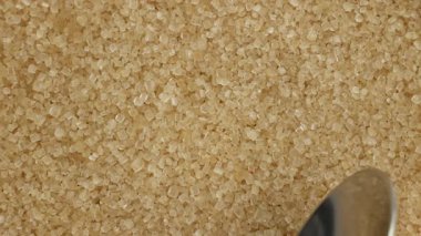 Yakın çekim videoda bir kaşık tarafından kepçelenen ham kahverengi şeker, yumuşak ışıklandırma altında dokuyu ve granüleritliği vurguluyor