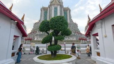 Tourists exploring Wat Arun temple in Bangkok, Thailand at sunset