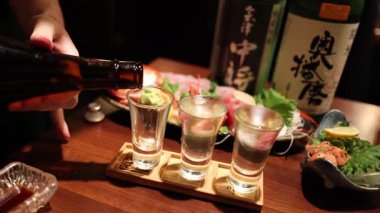 Sequential sake pouring into glasses at a bar