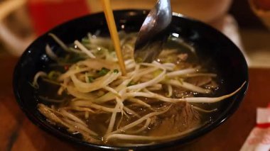 Close-up of a steaming bowl of Vietnamese pho with chopsticks and spoon, capturing rich textures and warm lighting