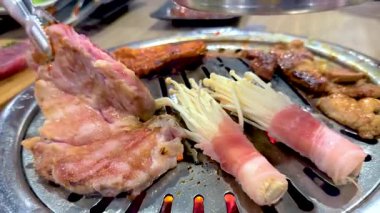 Close-up of Korean BBQ grilling meat and mushrooms on a tabletop grill in a Bangkok restaurant. Bright lighting enhances the vibrant colors