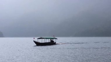 A boat moves steadily across a foggy lake.