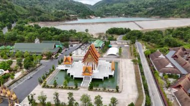 Drone footage captures a serene Buddhist temple in Phuket, Thailand, surrounded by lush greenery and tranquil water bodies