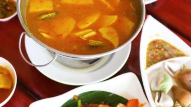 A vibrant display of Thai seafood dishes, including soup and fried squid, served on a wooden table in natural light
