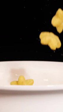Star-shaped cereal pieces fall into a white bowl against a black background, captured in slow motion with dramatic lighting