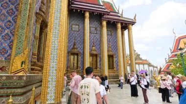 Tourists explore the vibrant Wat Phra Kaew Temple in Bangkok, Thailand, under bright daylight, capturing the temple's intricate architecture