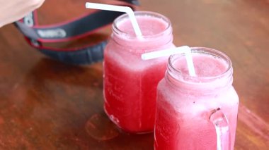 Two mason jars of vibrant watermelon juice on a wooden table in bright daylight, capturing a tropical refreshment moment
