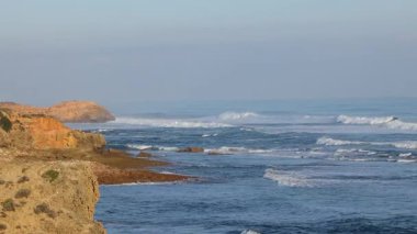 Waves crashing against rocky coastline at sunset