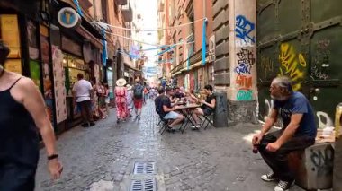 İnsanlar dar bir sokakta yürüyor ve yemek yiyorlar.