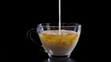 Süt, bir bardak çaya karışıp girdap desenler oluşturur. Dramatik ışıklandırma ile siyah bir arkaplan karşısında yakalandı