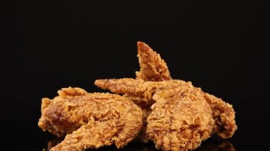 İştah açıcı doku ve detay için yumuşak stüdyo ışıklarıyla aydınlatılmış, parlak siyah bir yüzey üzerinde pürüzsüz bir şekilde dönen kızarmış tavuk kanatları.