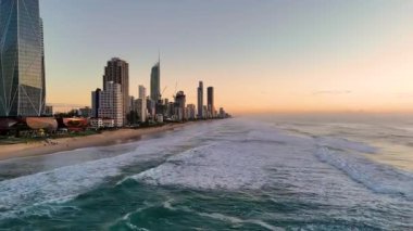 Güneş doğarken Gold Coast 'un ufuk çizgisinin havadan görünüşü, sıcak, altın ışık altında okyanus dalgalarını ve canlı şehir manzarasını yakalıyor.