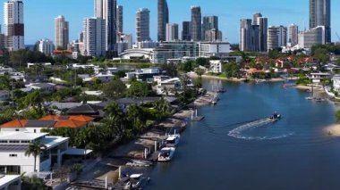 Bir tekne arka planda şehir silueti olan manzaralı bir su yolunda yol alır. Altın Sahili, Avustralya 'da gün ışığı altında.