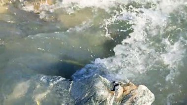Temiz su, kayaların üzerinden doğal bir derede akar. Parlak gün ışığında dinamik bir hareket ve doku yaratır.