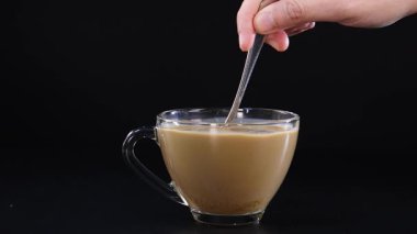 Bir el, bir bardak bardakta kahve ve süt karışımını siyah arka planda karıştırır.