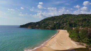 Drone görüntülerinde Phuket, Tayland 'da yemyeşil yemyeşil ve açık mavi gökyüzü altında sakin bir sahil görüntüsü var.