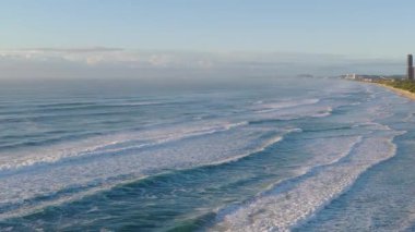 Okyanus dalgalarının yumuşak sabah ışığı altında Gold Coast plajına inişi sakin sahil güzelliğini vurguluyor.