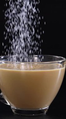 Şeker tanecikleri bir bardak kahveye dönüşür. Koyu bir zemine kurulur ve dinamik bir görsel efekt yaratır.