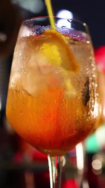 Bir saplı bardaktaki soğutulmuş portakal kokteylinin yakın çekimi canlı bar ışıkları, yoğunlaşma ve turunçgil süslemesi altında sarı bir çubukla karıştırılır.