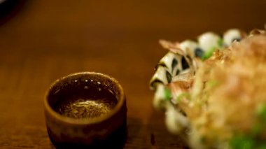 Elin yemeğin yanında sake bardağına uzanıyor.