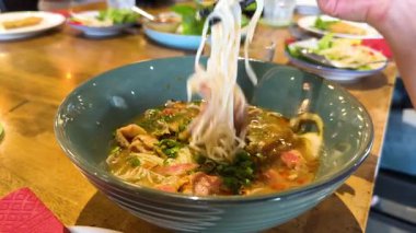 Çubuklar, Bangkok 'ta canlı bir restoranda, buharda pişen bir kase sığır etinden pirinç eriştesi kaldırır.