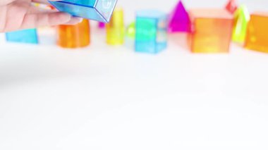 Eller, beyaz bir tablo üzerinde yarı saydam 3D şekilleri manipüle ederek, parlak, eğitici bir ortamda geometri ve renkleri vurguluyor