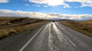 Bir karavan, kırsal alanda ıslak bir yolda dramatik bulutlar ve parlak sonbahar güneşinin altında ilerler.