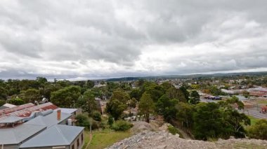 Ballarat 'ın geniş bir hava manzarası, yemyeşil ve şehir yapılarını sergiliyor bulutlu bir gökyüzü altında, dinamik bir hareketle yakalanıyor.